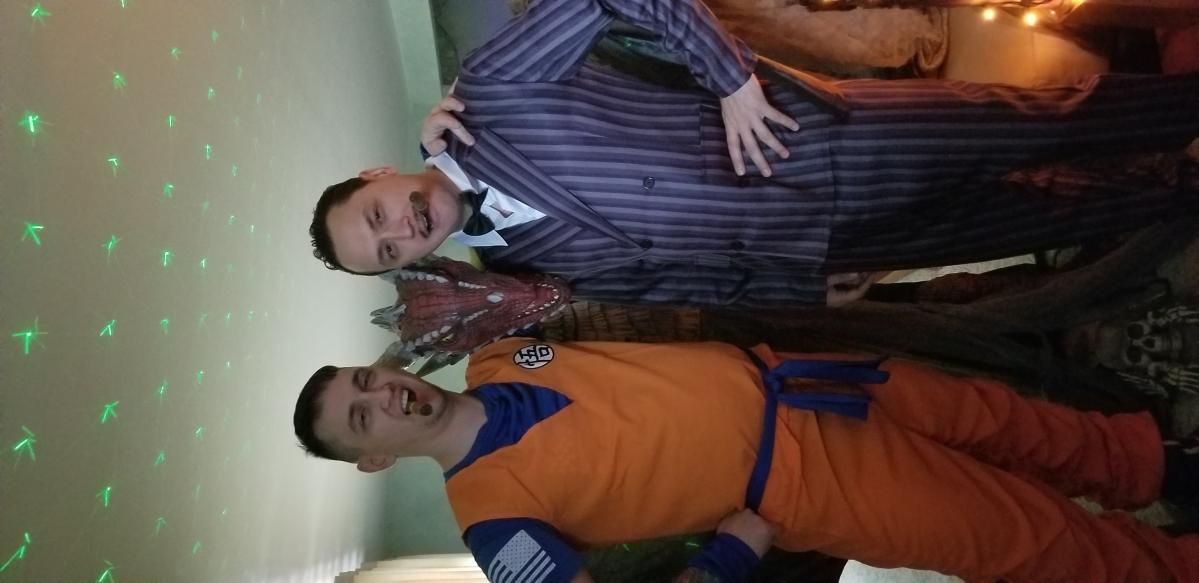 Indoor party customer shot by @Moto, Gomez Addams cosplayer in stripe suit posing with another cosplayer, festive halloween scene