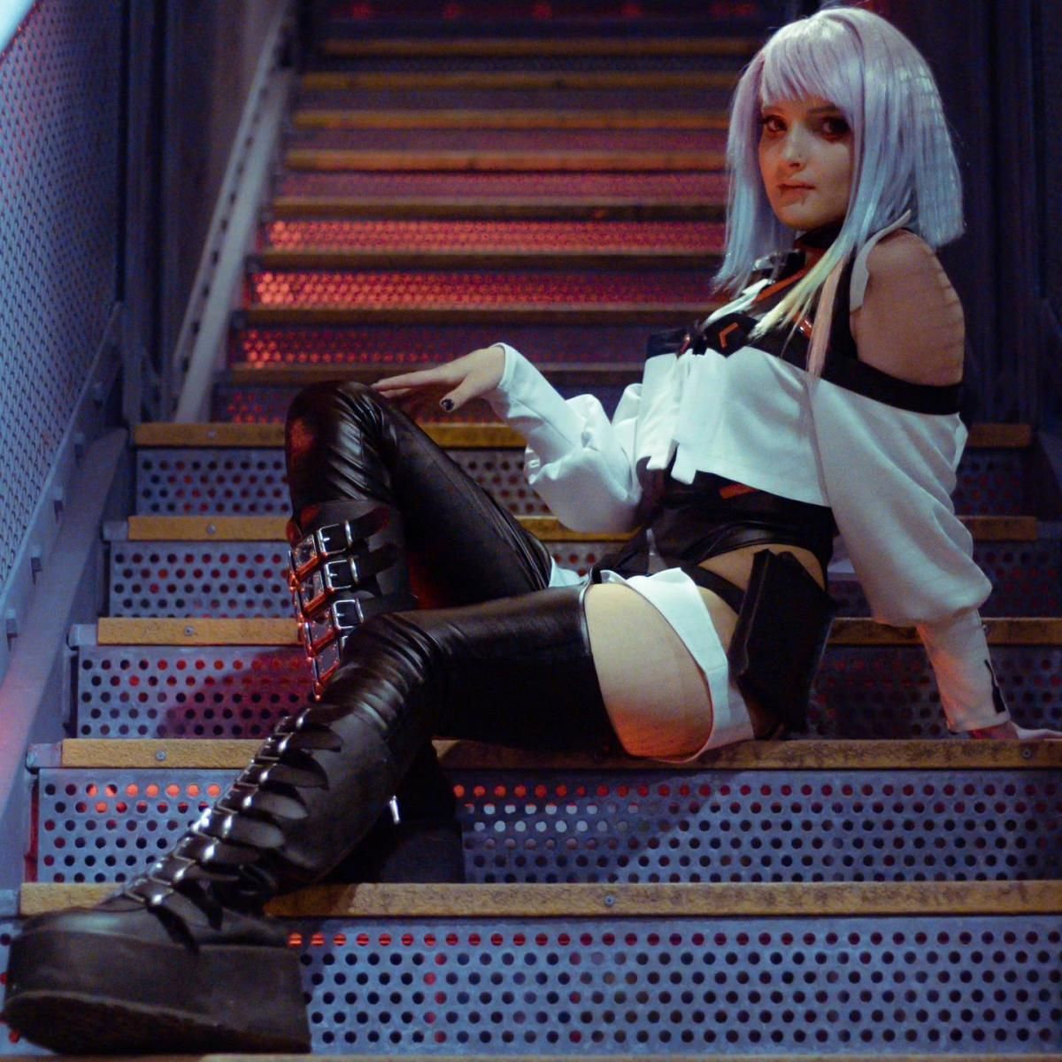 Outdoor customer full-body shot taken by @Ἔρως sitting on perforated industrial stairs, showing off detached puffy white sleeves, waist tactical pouch and detailed buckle thigh-high boots