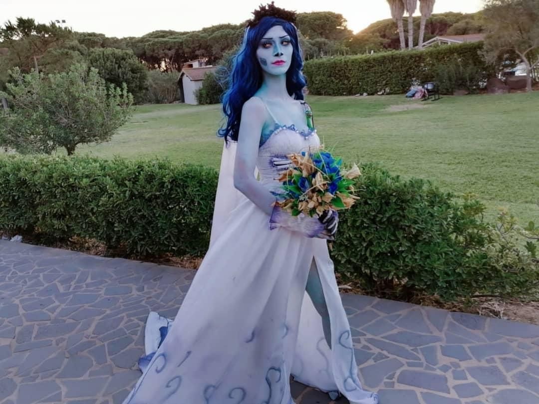 Outdoor sunset customer full-body portrait by @aiiro, full Emily ghost bridal set including gradient printed sheer wedding gown, floral head wreath, skeleton printed long gloves and matching blue gradient wig, holding handmade blue dead flower bouquet on stone paved garden path
