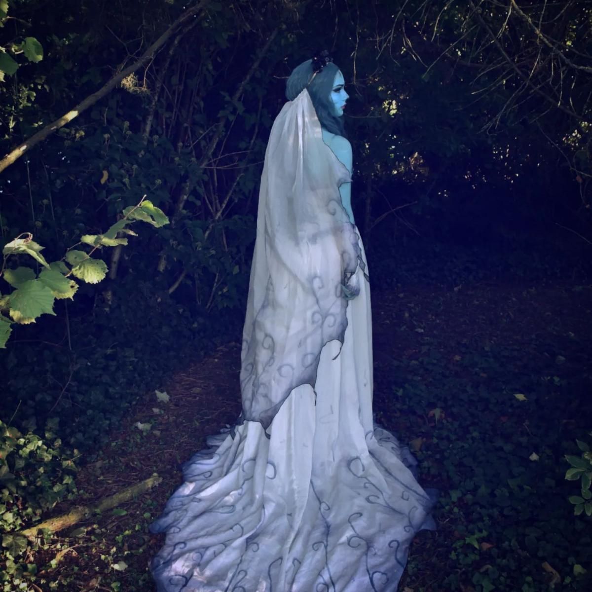 Back view full trail outdoor shot of @Camille standing on leafy forest path, showcasing full swirling vine gradient print covering entire long train of the ghost wedding dress, flowing layered veil trailing down the back