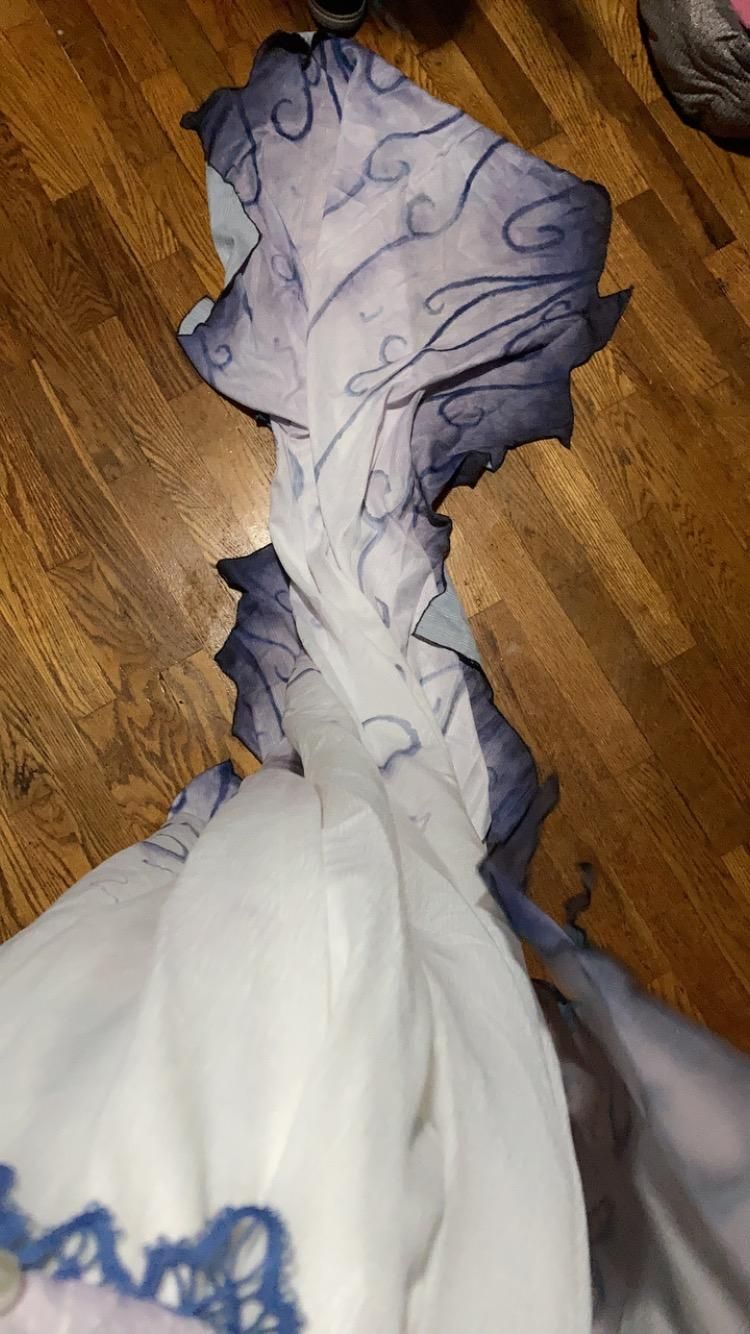Flat lay unboxing shot of Emily’s full jagged chiffon train on solid wood floor, complete continuous dark swirling vine gradient ink print, asymmetrical tattered irregular skirt edge, blue lace trim at front corset hem