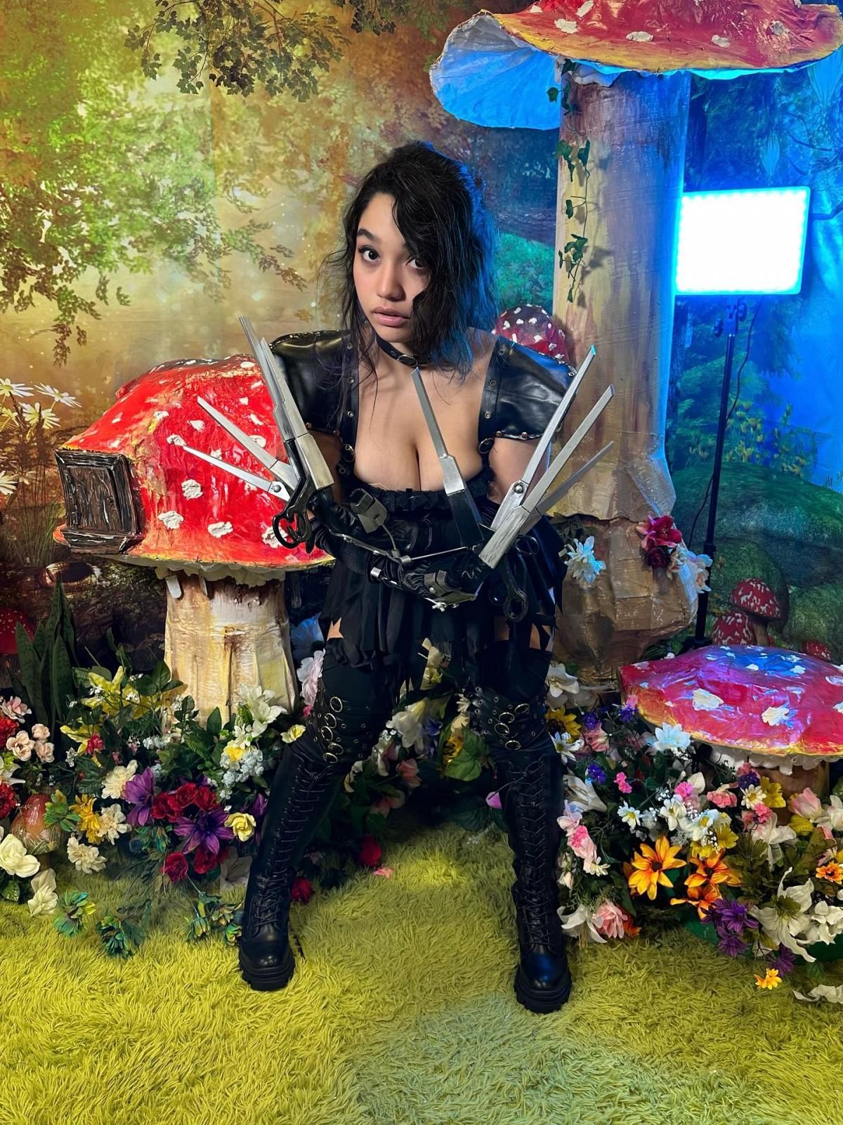 Full‑body customer cosplay shot by @princessa_jaq against whimsical mushroom forest backdrop, complete gender‑bend Edward Scissorhands outfit with scissor‑hand props, black gothic dress and thigh accessories