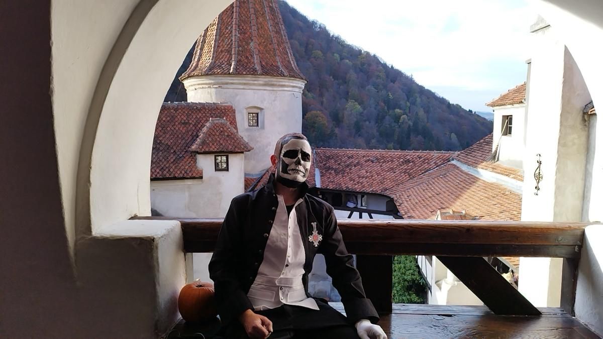 Outdoor castle balcony cos photo by @Barron, Papa Emeritus sitting pose with embroidered coat badge, vintage medieval building background and pumpkin prop