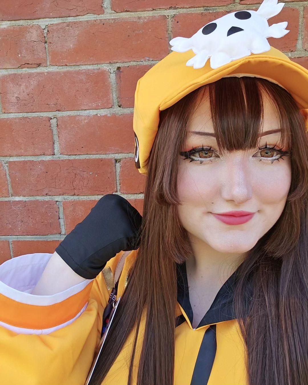 Close-up halfbody customer cosplay shot of May from Guilty Gear Strive by coser @Kiri, full orange hoodie costume with skull beret, brown long wig and black fingerless gloves