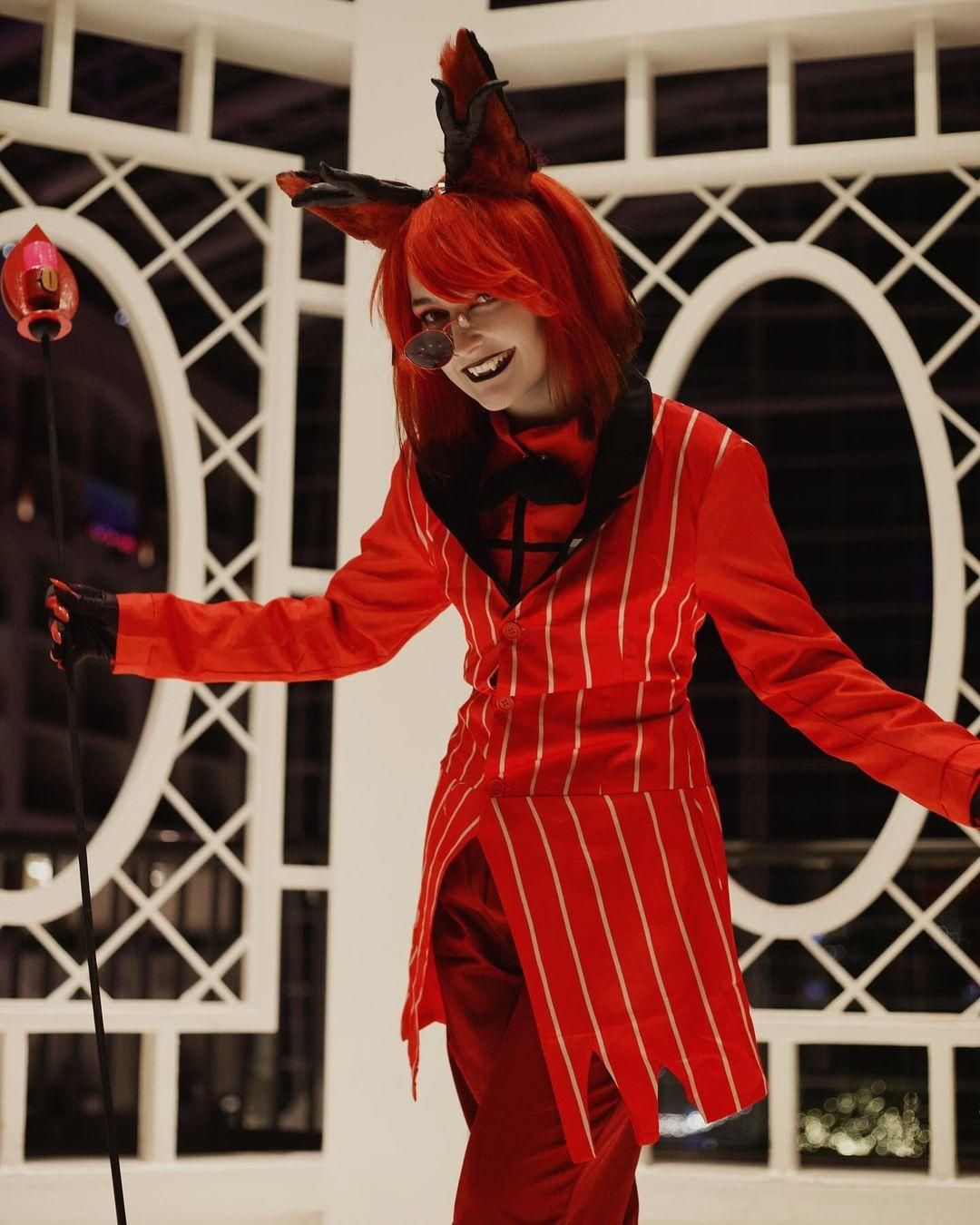 Night outdoor half-body dynamic shot of @zeni.cos with arms outstretched in front of white lattice architecture, full Alastor red pinstripe outfit, black collar detail, styled red wig, claw gloves, radio staff prop placed on side, night city bokeh background