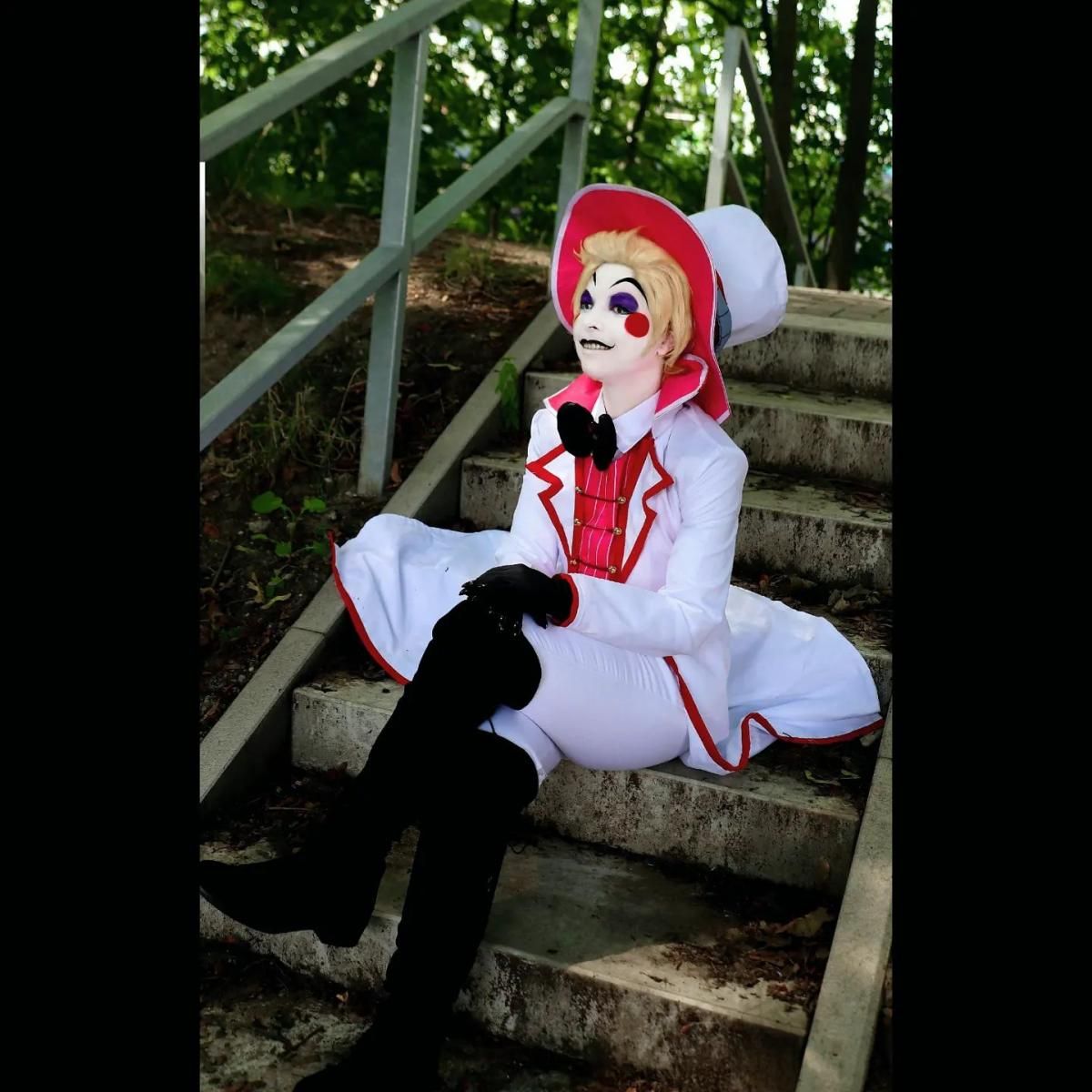 Full-body sitting shot of @cantarella_creative on outdoor forest stone stairs, full Lucifer cos suit layered display: white long tailcoat with red jagged hem, red pinstripe vest, black bow tie, loose white trousers with red cuffs, tall black knee-high leather boots, matching top hat and black gloves, green forest natural background