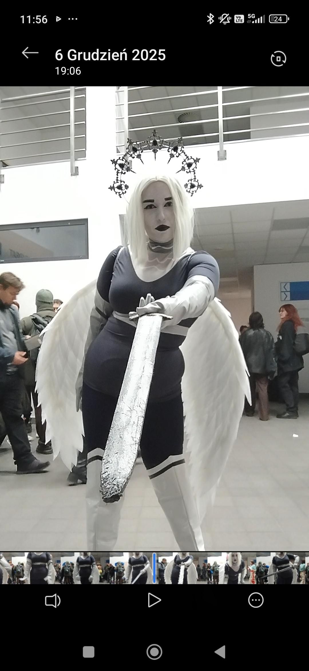 Indoor convention customer shot by @Brb, full Lute exterminator uniform, white wig, angel halo and wings, holding prop sword facing camera