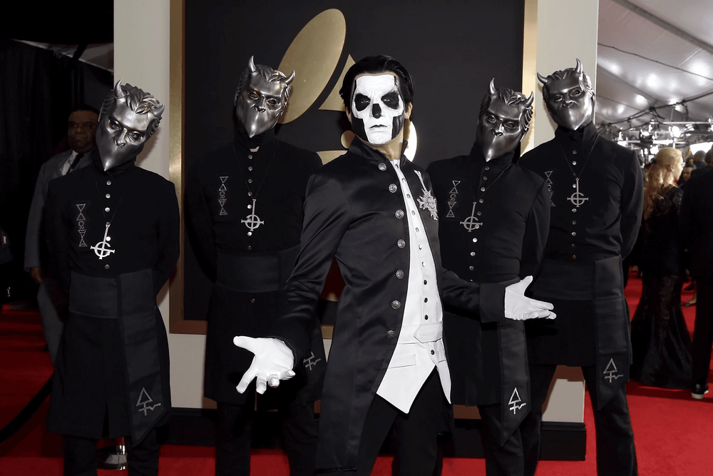 Official Grammy red carpet photo of Ghost band, Papa Emeritus center stage with signature skull makeup and black-and-white tailcoat suit, surrounded by masked Nameless Ghoul band members