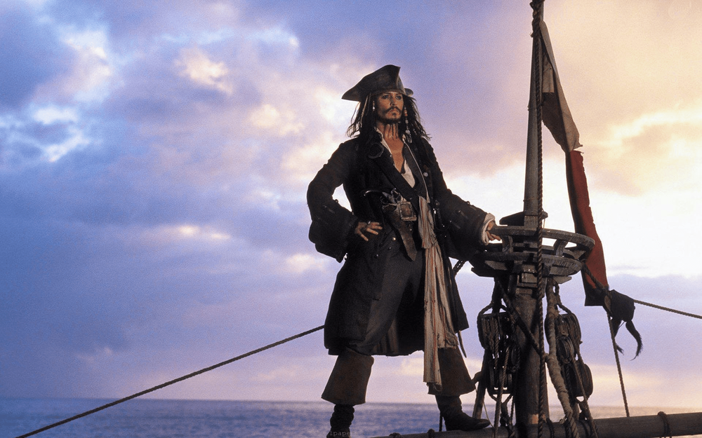 Official movie still of Captain Jack Sparrow standing on pirate ship deck at dusk, full iconic costume styling for cosplay reference