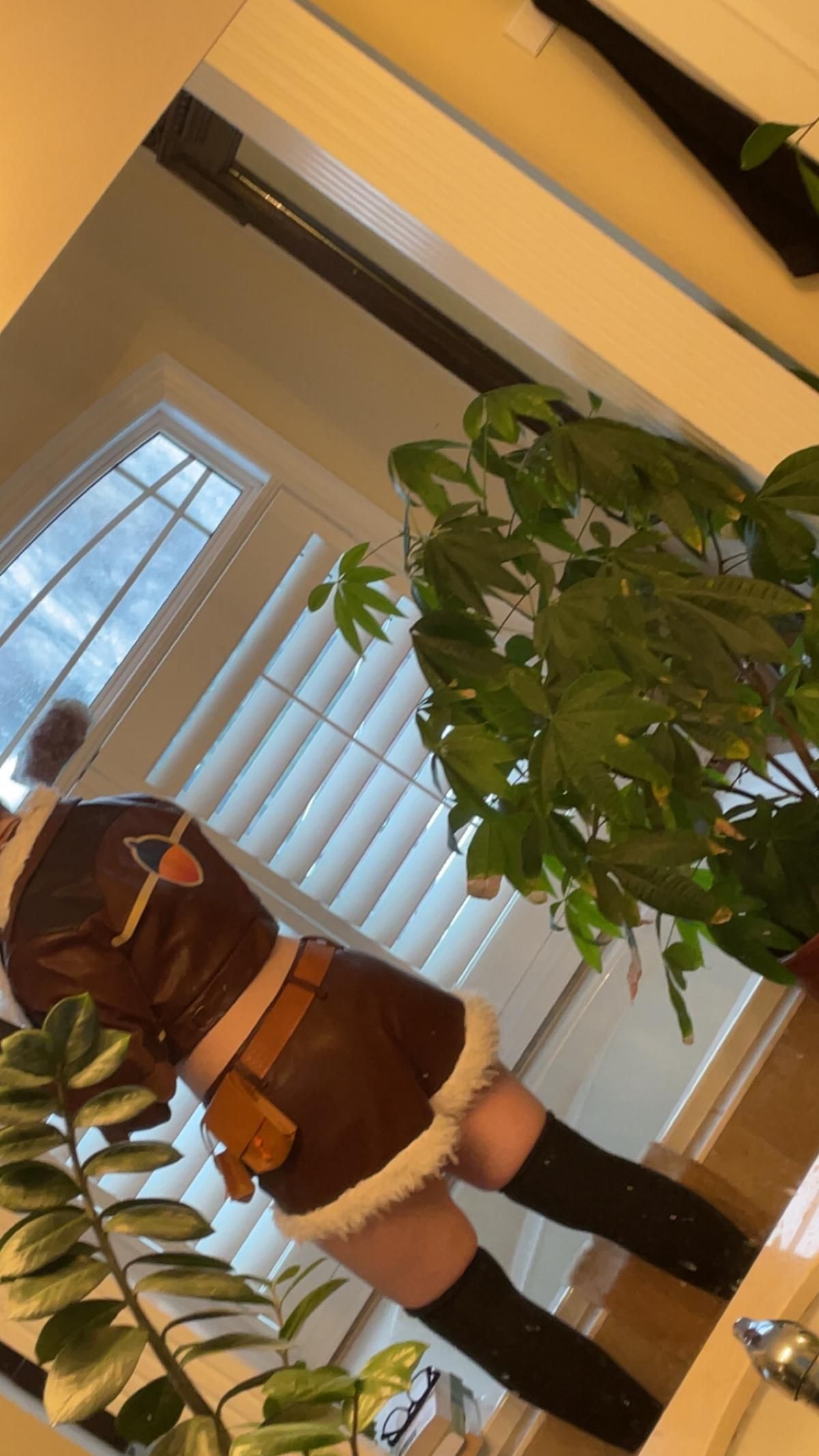 Back view customer mirror selfie of Squirrel Girl cosplay, showing jacket back patch, short pants cut, belt pouches and thigh‑high stocking match, indoor home scene