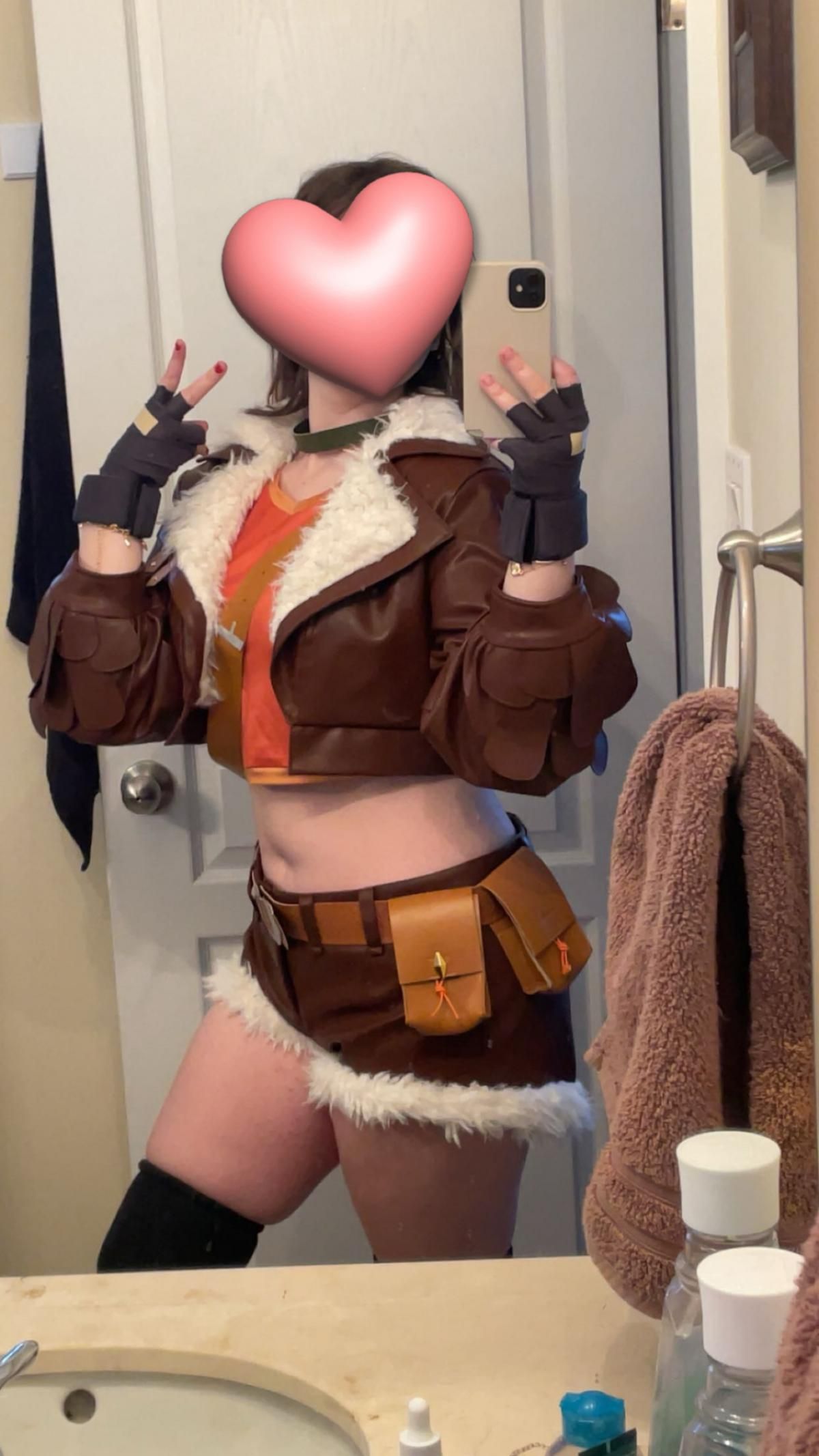 Customer @reece full‑body mirror selfie of Squirrel Girl cosplay, brown fur‑trimmed cropped jacket, orange crop top, fur‑edged shorts and fingerless gloves, indoor bathroom setting