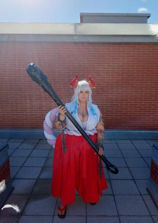 Full‑body outdoor cosplay photo by @aerenchan, One Piece Yamato costume with red hakama, big club prop, horns and thick rope accessory on rooftop.