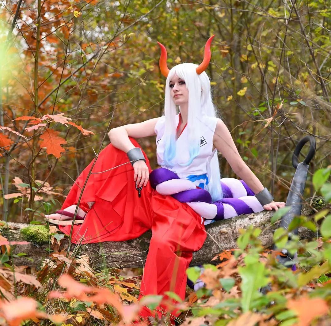 Relaxed sitting cosplay shot by @corvus.cosplay on fallen log in autumn woods, One Piece Yamato full outfit with shackles and rope ornament.