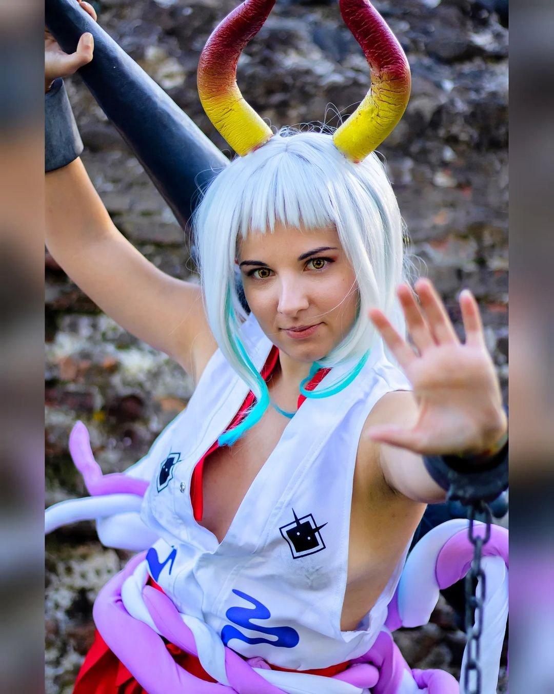 Outdoor stone wall cosplay shot by @GiaDi Rox as One Piece Yamato, gradient horns, holding kanabo club, shackle chains, white sleeveless top and red hakama.