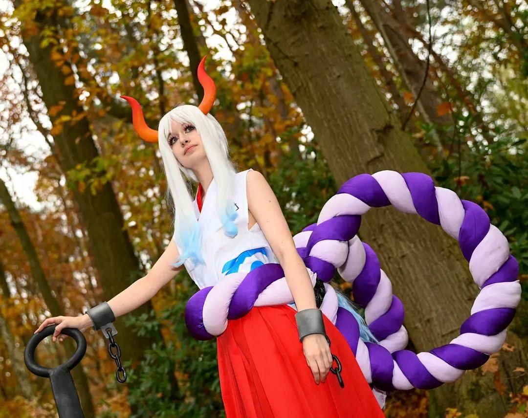 Side‑pose outdoor cosplay photo by @corvus.cosplay in autumn woodland, One Piece Yamato holding kanabo club prop, oversized purple‑white rope around waist.