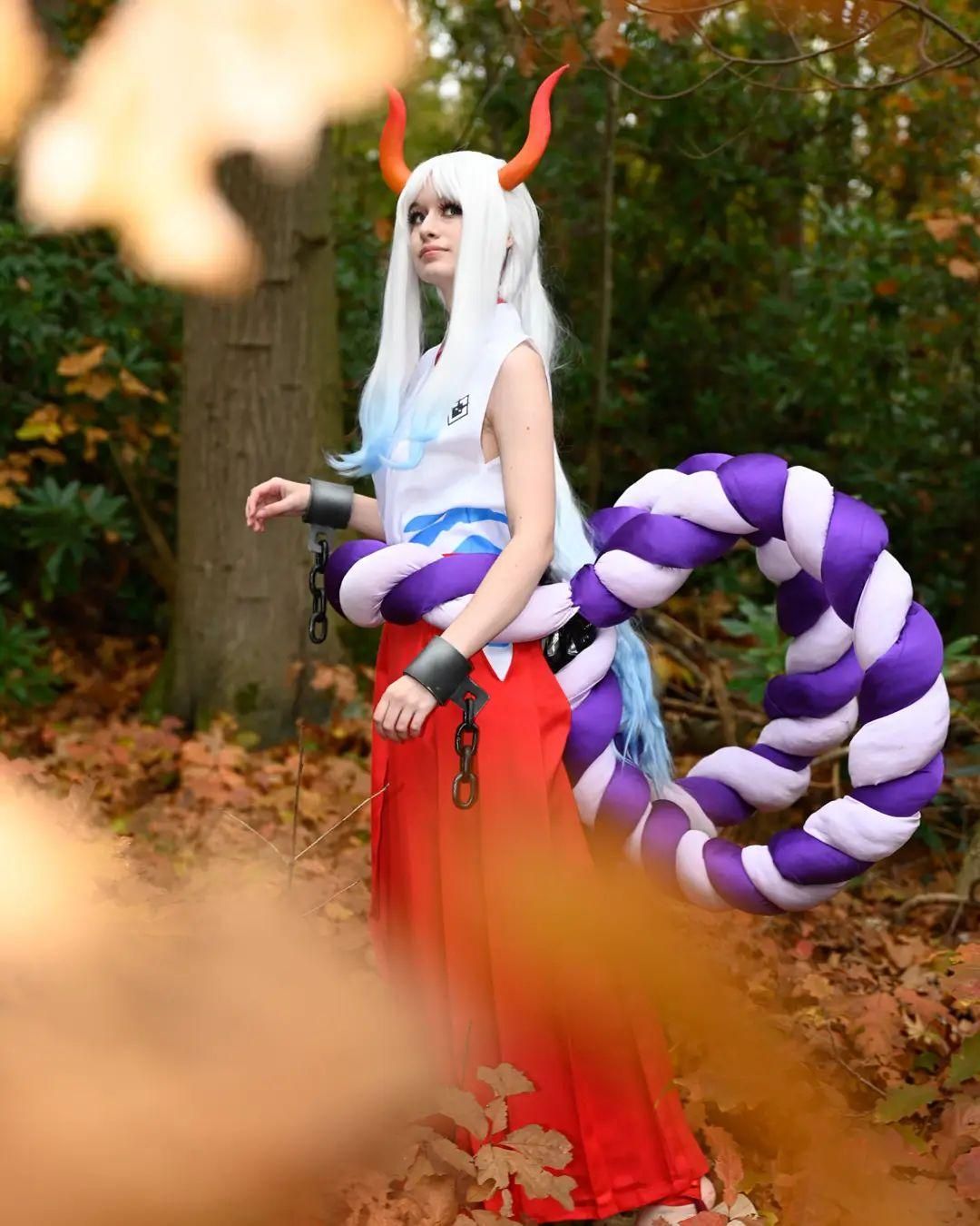 Outdoor autumn forest cosplay shot by @corvus.cosplay as One Piece Yamato, gradient horns, shackle chains, huge purple‑white rope accessory, white top and red hakama.