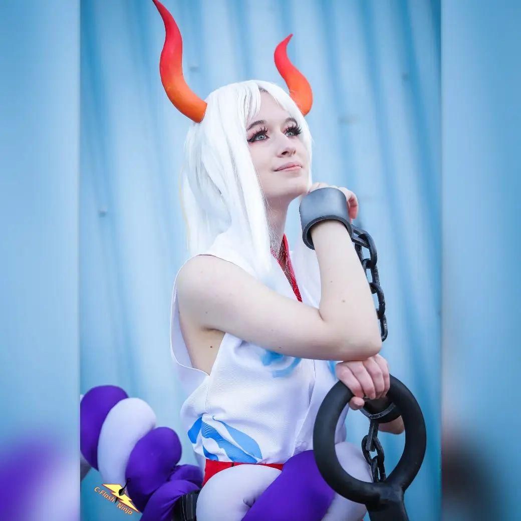 Half‑body close‑up cosplay shot by @corvus.cosplay, One Piece Yamato against light blue backdrop, horns, shackles and part of kanabo club prop are visible.