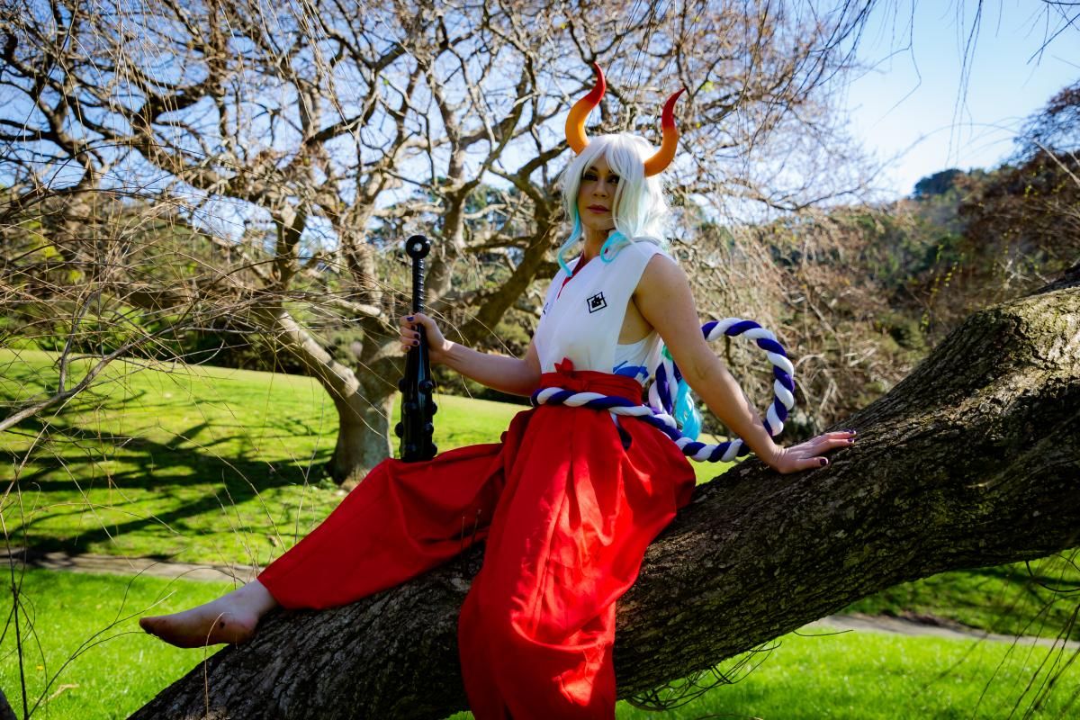 Outdoor park cosplay shot by @Ella Day for One Piece Yamato, sitting on big tree branch, holding kanabo club prop, white‑blue rope and red hakama.