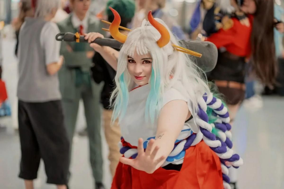 Anime convention floor cosplay shot by @jennis_cosplays as One Piece Yamato, dynamic hand gesture, kanabo prop over shoulder, horns and big rope accessory.