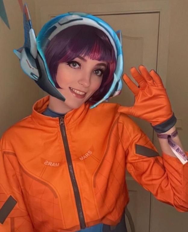 Second indoor customer photo from @aliceintokkiland with friendly waving gesture, clearly showing the layout of sleeve dark patches and front chest text prints on the orange jacket
