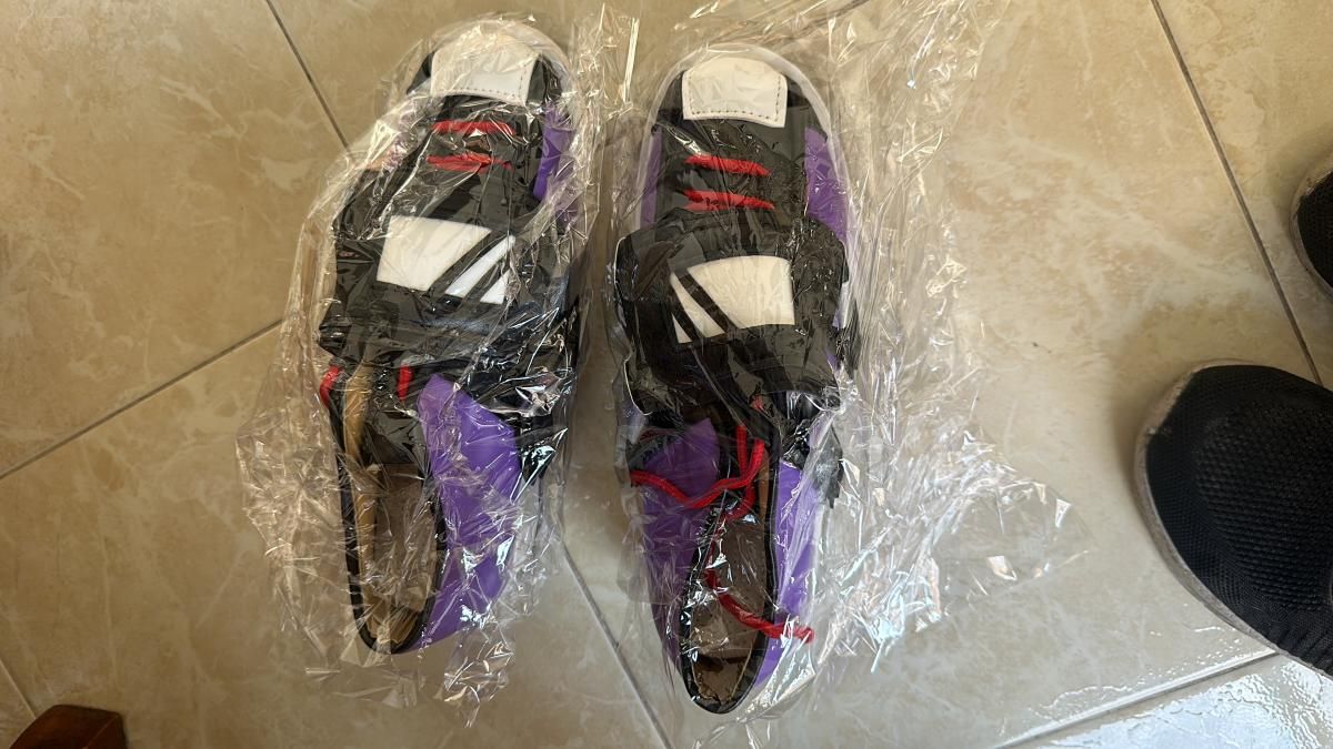 Pair of ISO themed high-top sneakers sealed in clear protective plastic, color block design of black, white, purple and red laces, layered panel stitching matching in-game footwear silhouette