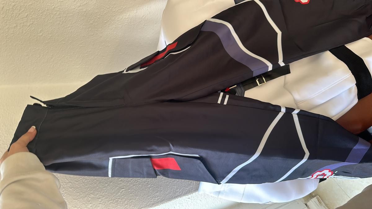 Flat lay unbox shot of ISO matching dark tactical cargo pants, printed white & purple geometric armor line art, dual side cargo pockets with red rectangular patch accents, ankle zipper cuffs